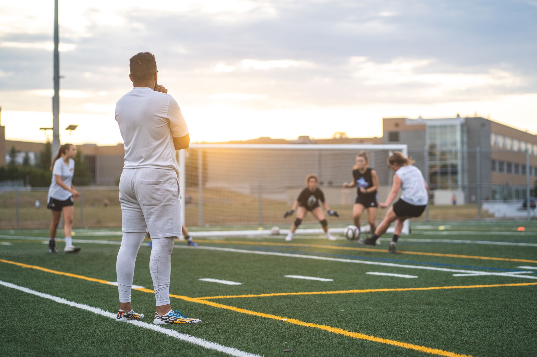 Groupe de femmes avec un entraîneur s'entraînant au football ensemble sur un terrain de sport avec des lignes sous un ciel ensoleillé et nuageux en été en contre-jour