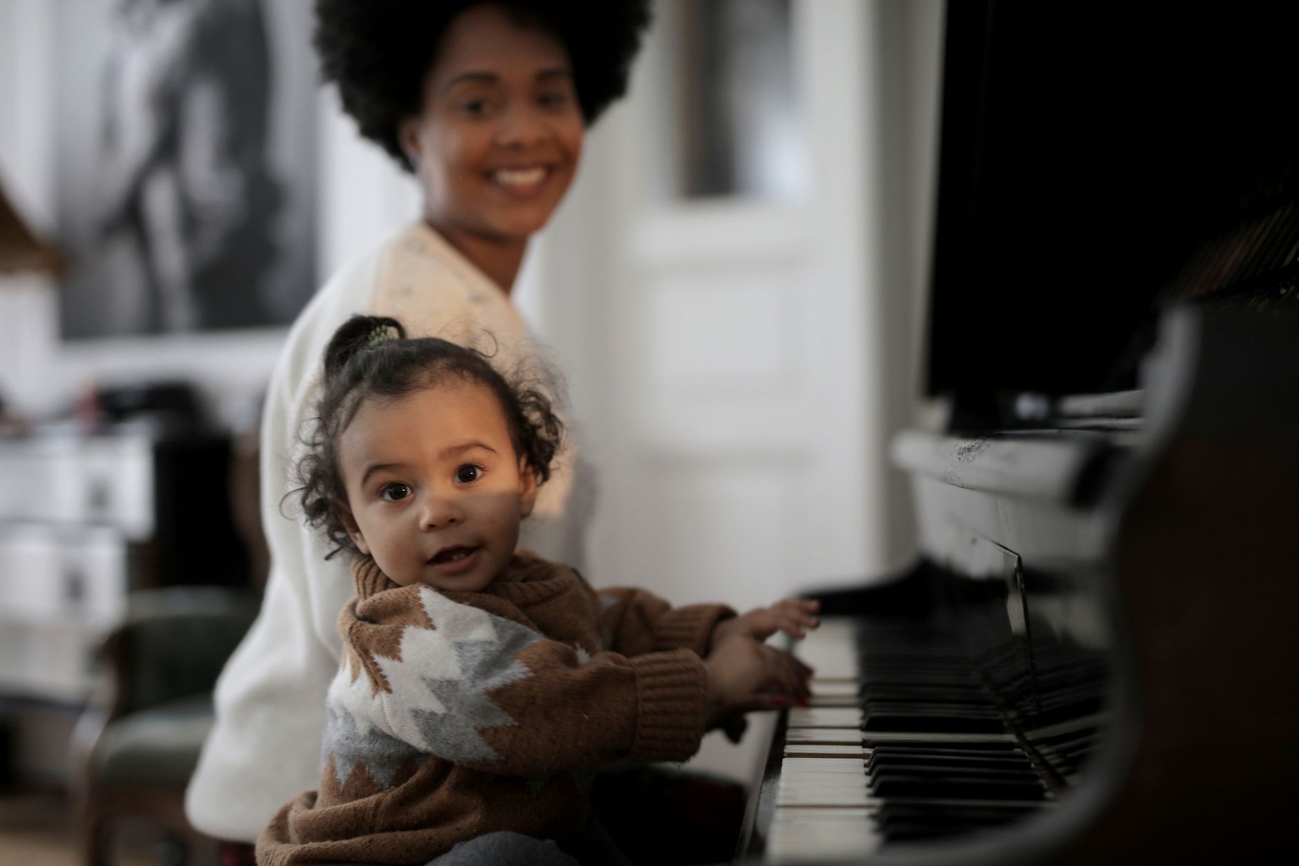 Adorable tout-petit jouant du piano avec un parent souriant en arrière-plan, capturant un moment familial chaleureux.