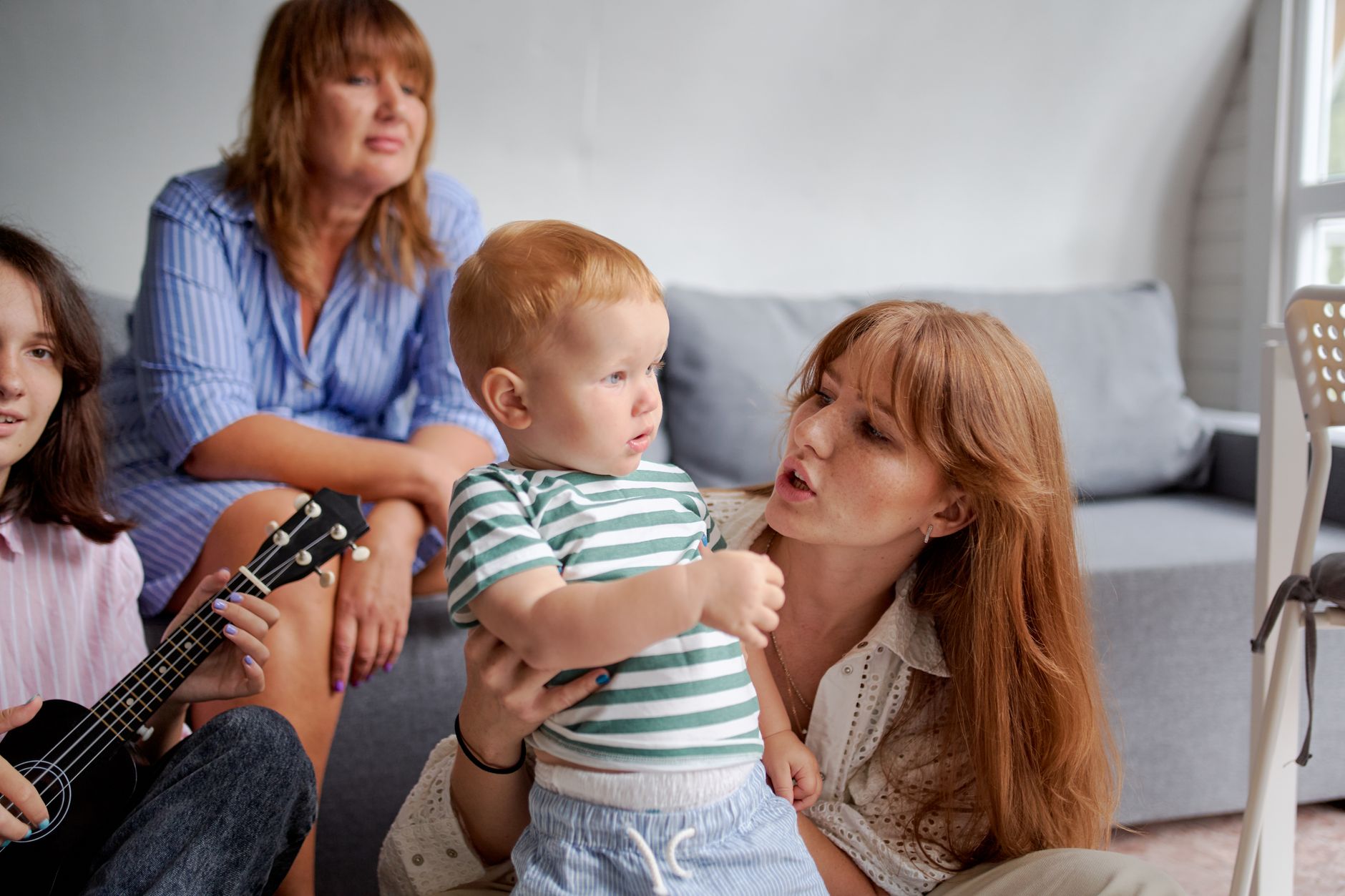 Des femmes avec un enfant en bas âge près de leur grand-mère et de leur sœur jouant du ukulélé tout en passant du temps ensemble le week-end