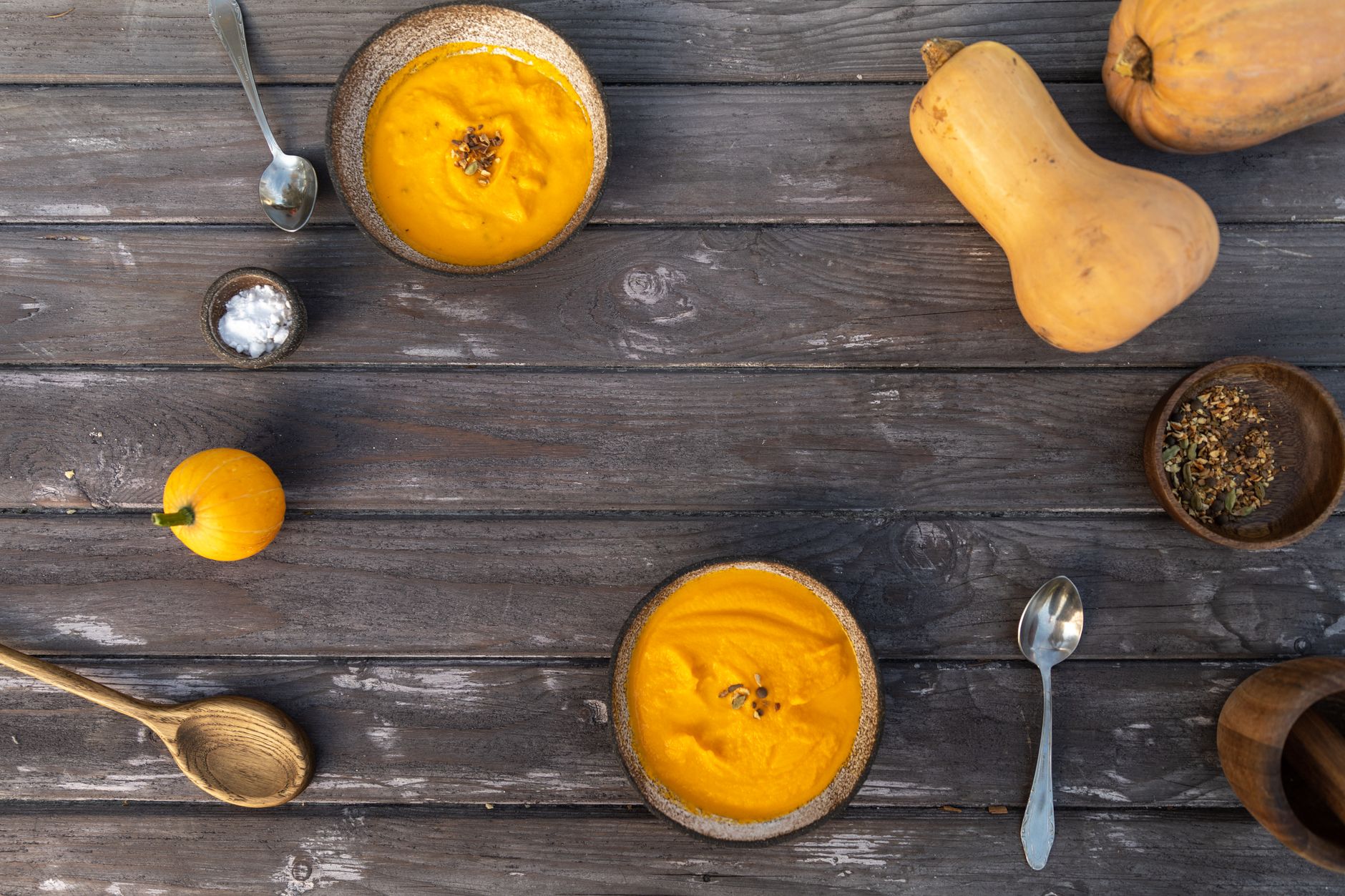 Bols de velouté de courge sur une table en bois, entourés de courges