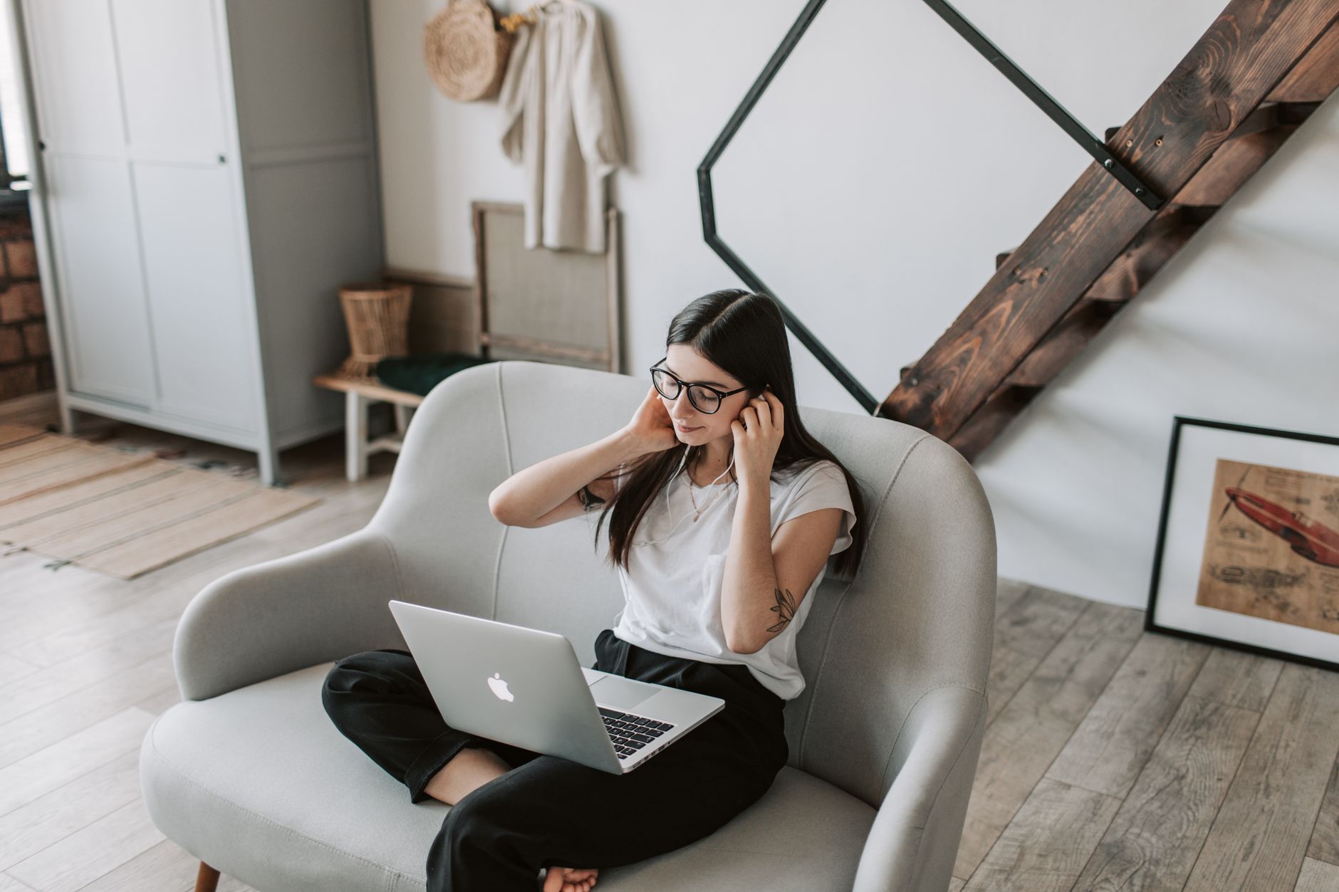 Une jeune femme portant des lunettes est assise dans un fauteuil avec un ordinateur portable sur ses genoux.